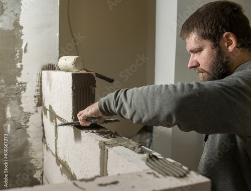 a male builder puts a wall of foam concrete blocks, he spreads a mortar for masonry with a spatula..