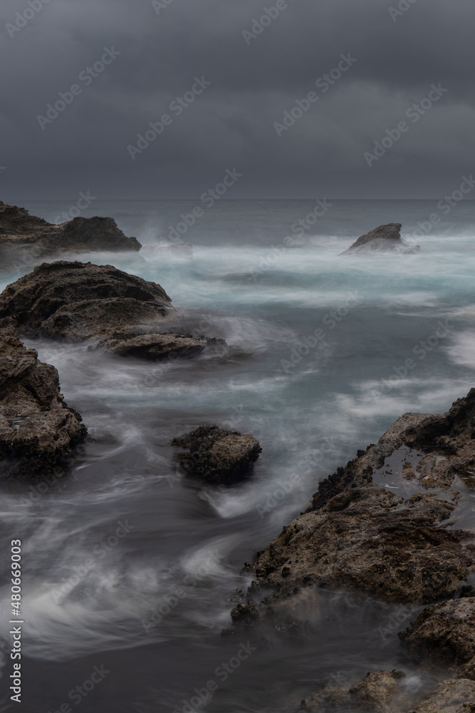 Ocean water flowing between rocks on the stormy day.
