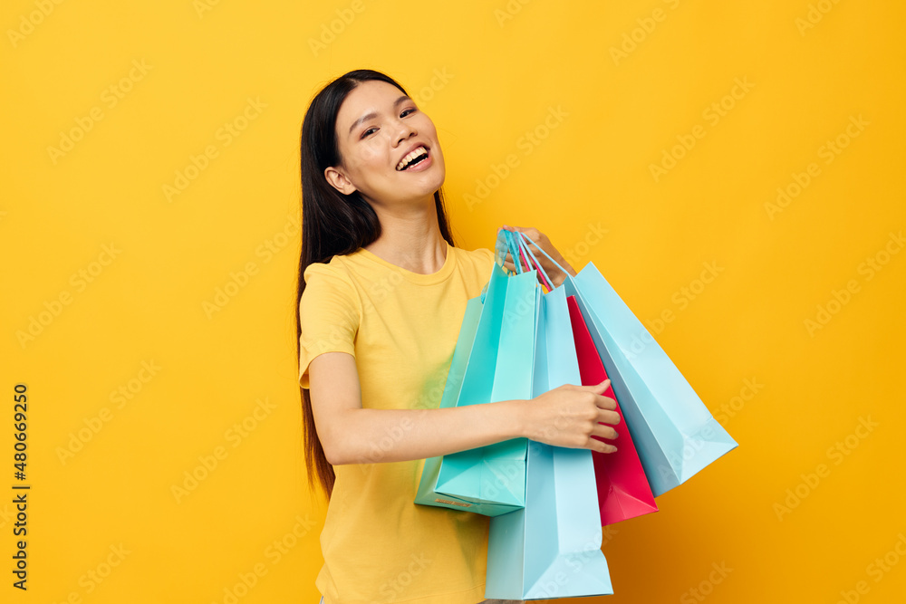 Portrait Asian beautiful young woman in a yellow T-shirt with multicolored shopping bags studio model unaltered Portrait Asian beautiful young woman in a yellow T-shirt with multicolored shopping bags studio model unaltered