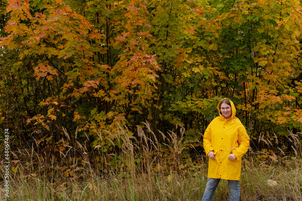 A cheerful young woman in a yellow raincoat and yellow boots on the background of an autumn landscape
