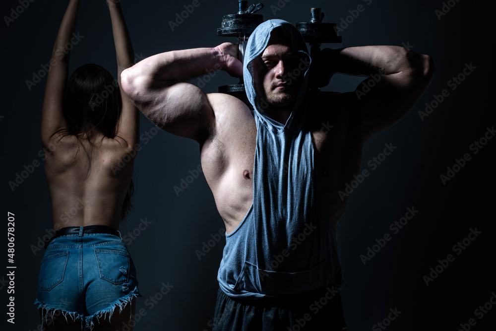 Sports people are working out with dumbbells. Fit couple doing exercise with dumbbells in dark studio.
