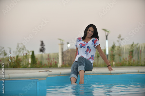 beautiful woman standing on the edge of the pool smiling. woman sitting with her feet in the pool.