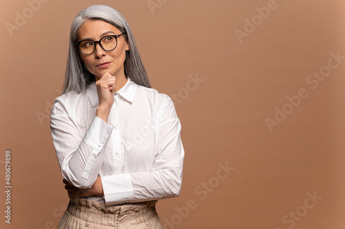 Obraz na plátně Smart and thoughtful mature woman holding her chin and pondering idea, making difficult decision, looking uncertain doubtful