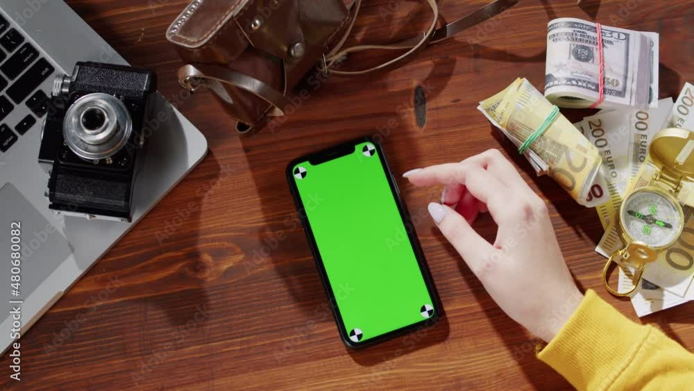 Woman using smartphone with chroma key top view, money cash, compass, photo camera and laptop computer on table. Traveling and tourism, mobile phone with green screen close-up. Woman using smartphone with chroma key top view, money cash, compass, photo camera and laptop computer on table. Traveling and tourism, mobile phone with green screen close-up.