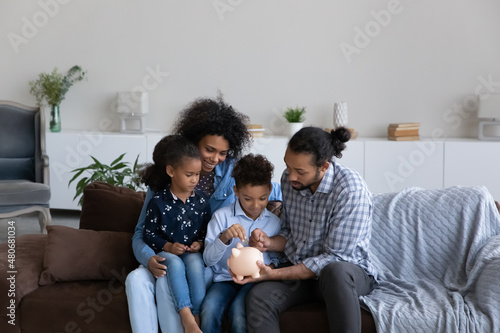 Foto Happy millennial African American parents teaching little sibling kids to save money, making reserve