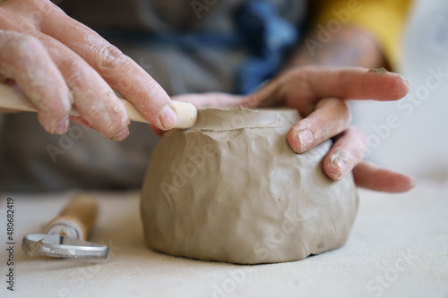 Creative handcraft process: female artist use tool for shaping and handmade sculpting of clay pottery. Workplace table in workshop with woman potter work with raw material creating handicraft ceramics