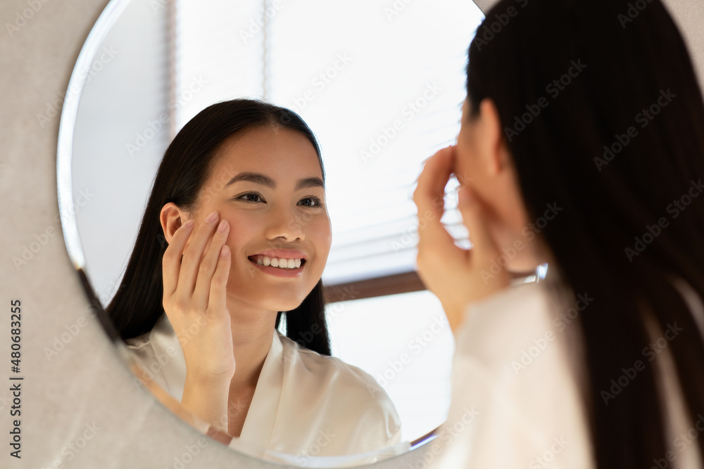Mirror reflection of happy asian woman applying eye care product Mirror reflection of happy asian woman applying eye care product
