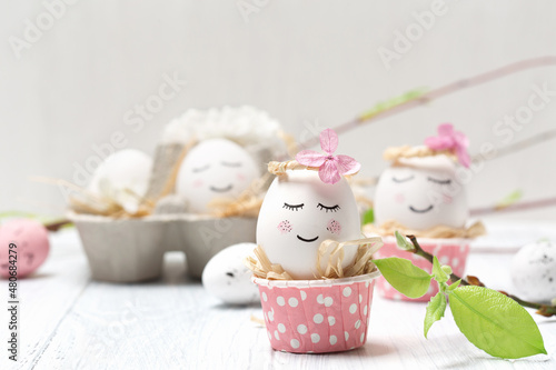 Easter holiday concept with cute handmade white eggs  tree branches  quail feathers and spring flowers on white wooden background.