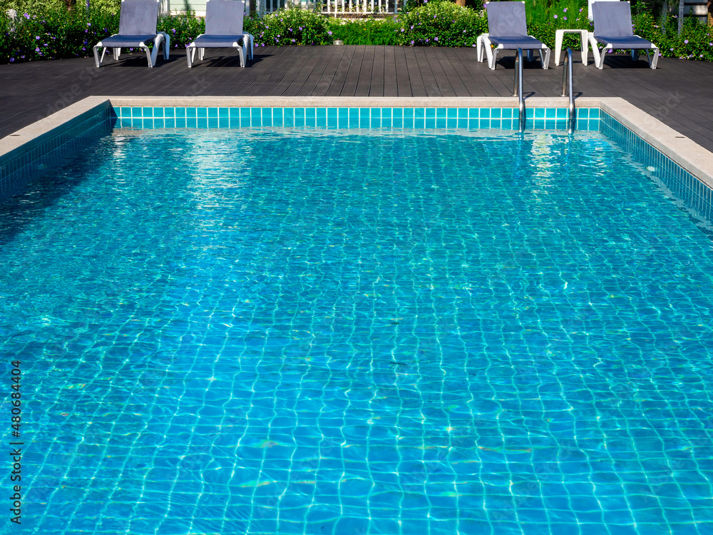 Swimming pool with clean clear water, nobody. Square shaped pool with blue tiles with grab bars ladder and sunbeds on the wood decks, no people. water surface. Overhead view.  Summer background.