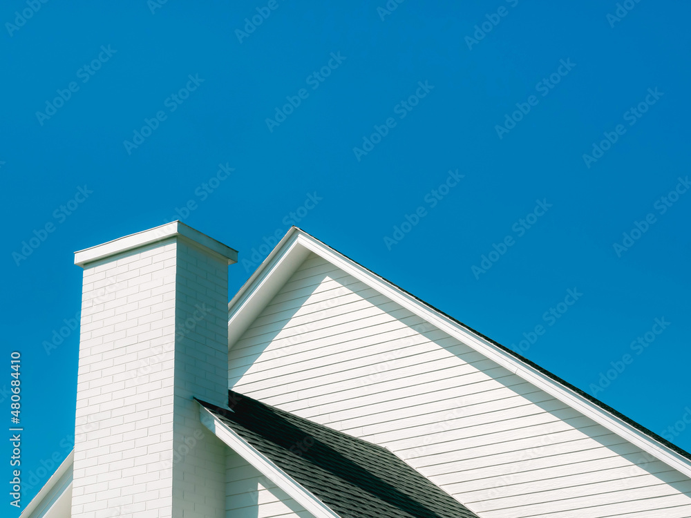 A white chimney bricks on the roof of the big wooden white house against blue sky background on a sunny day with copy space.