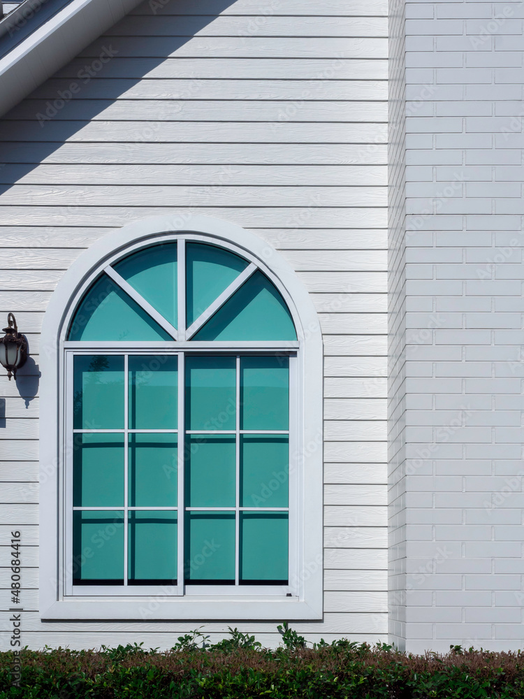 A white house window with glass, curved frame, green curtain decoration on the big white wooden resident, vertical style, view from outdoor. A white house window with glass, curved frame, green curtain decoration on the big white wooden resident, vertical style, view from outdoor.