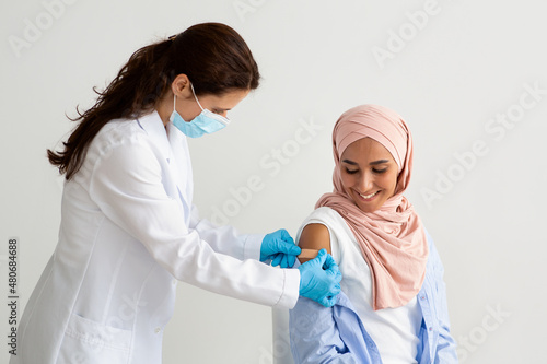 Doctor Applying Sticking Plaster On Muslim Woman's Shoulder After Vaccine Injection Shot