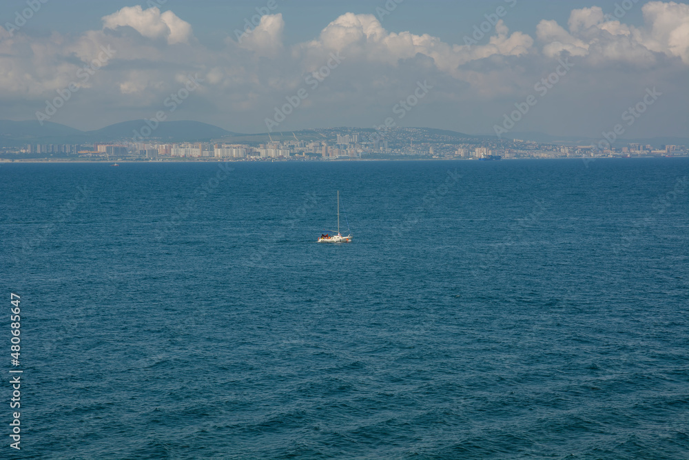 a lonely yacht on the background of the ocean and blue sky with clouds