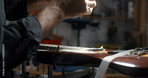 Luthier covers guitar body with masking tape before sanding the frets at his shop. Care and repair of the muscial instruments, 4k 60p Prores HQ photo
