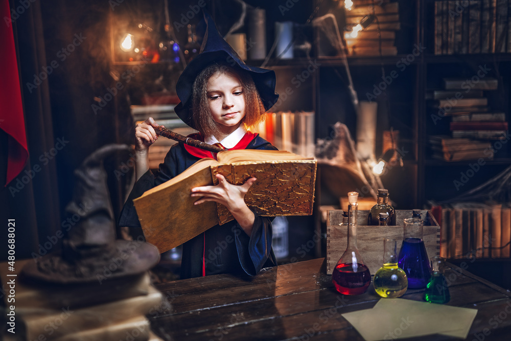 Fototapeta premium Little witches reads magic book while holds magic wand. Halloween party. Cosplay Harry Potter