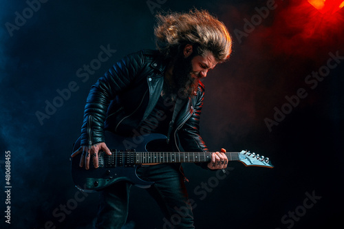 Expressive man rock guitar player with long hair and beard plays on the smoke background. Studio shot