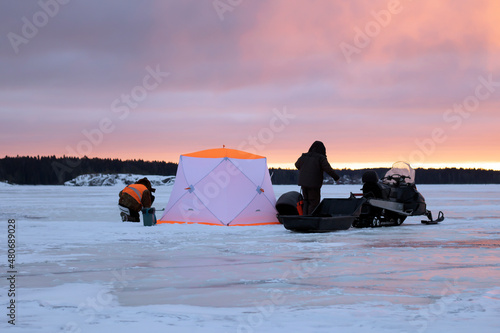 Ice fishing tent and snowmobile with fishermen. Landscape winter. Ice fishing is a popular sport.