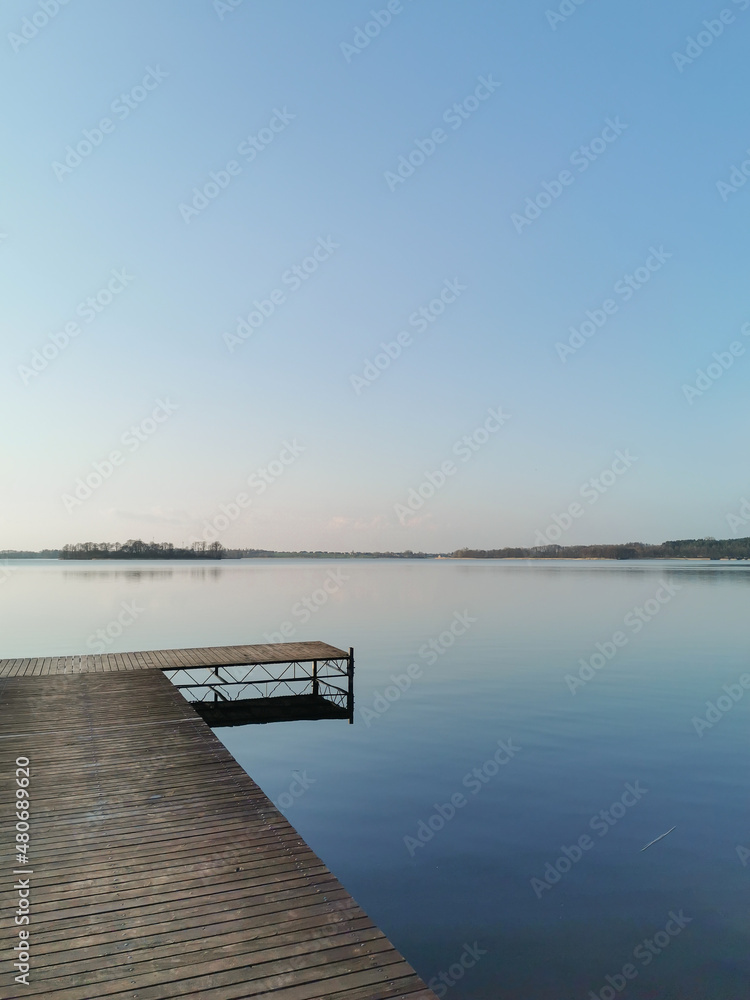Lake view with a wooden pier in the lower left corner. Blue sky and water at the dusk. Calm scene of nature and nobody.