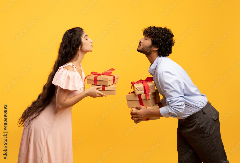 Romantic indian lovers exchanging gifts for Valentine's Day or anniversary, trying to kiss each other, side view Romantic indian lovers exchanging gifts for Valentine's Day or anniversary, trying to kiss each other, side view