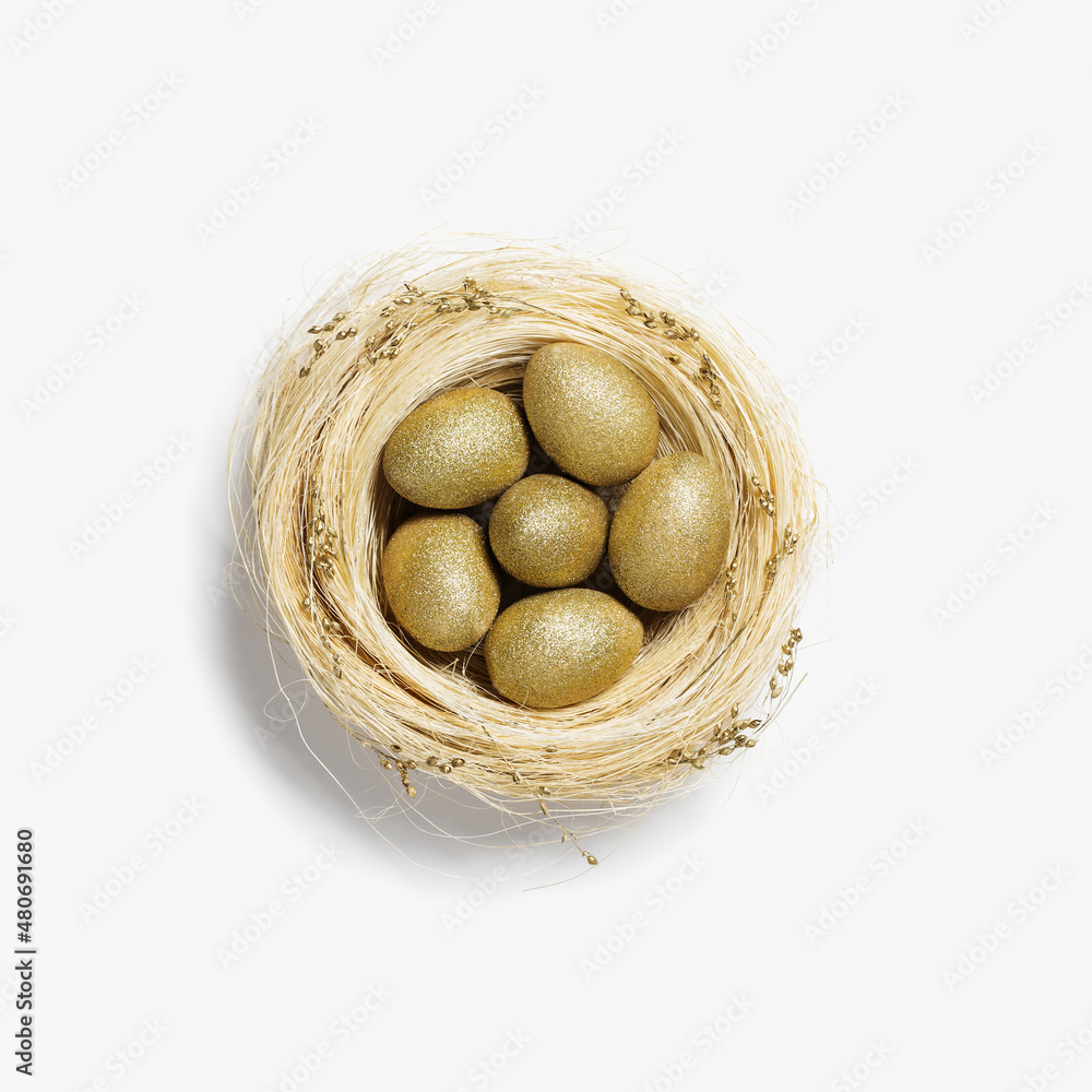 Golden color eggs in nest from straw on white background. Stylish gold egg for easter spring holiday. Top view decorative shiny Easter eggs minimal style card Golden color eggs in nest from straw on white background. Stylish gold egg for easter spring holiday. Top view decorative shiny Easter eggs minimal style card