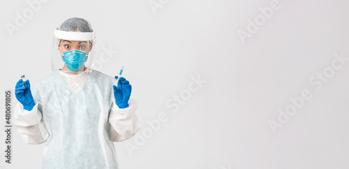 Covid-19, coronavirus disease, healthcare workers concept. Amazed and excited female asian doctor, infectionist in personal protective equipment, holding syringe and ampoule with vaccine photo