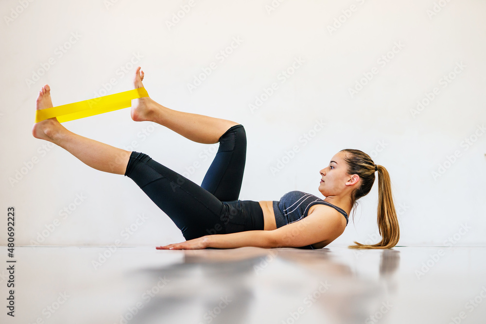 Young caucasian woman fitness instructor training in front of white wall with rubber resistance band - full length sporty female with copy space side view Young caucasian woman fitness instructor training in front of white wall with rubber resistance band - full length sporty female with copy space side view