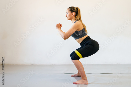 Young caucasian woman fitness instructor training in front of white wall with rubber resistance band - full length sporty female with copy space side view