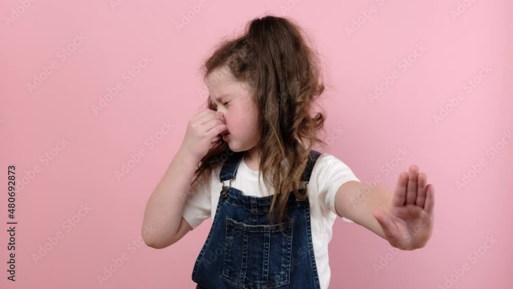 Portrait of little girl kid grabbing nose with fingers, feeling unpleasant smell, shocked with disgusted fart, posing isolated over pink color background wall in studio. People emotion concept Portrait of little girl kid grabbing nose with fingers, feeling unpleasant smell, shocked with disgusted fart, posing isolated over pink color background wall in studio. People emotion concept