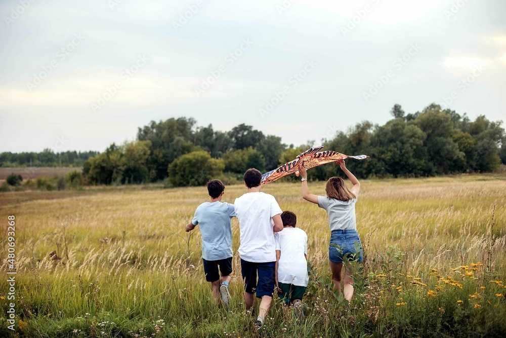 A young family of four runs across the field and flies a kite at sunset in the summer.