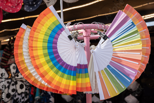 Hand fan painted in the colours of the pride flag hanging on a coat rack
