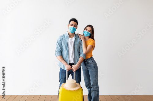 New travel rules. Loving couple in face masks, standing with luggage ready for vacation trip during coronavirus pandemic