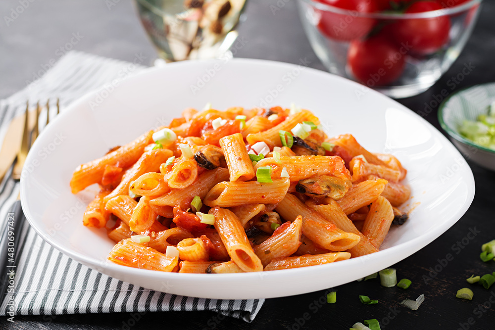 Classic italian pasta penne marinara with mussels and green onions on dark table. Penne pasta with sauce marinara. Classic italian pasta penne marinara with mussels and green onions on dark table. Penne pasta with sauce marinara.