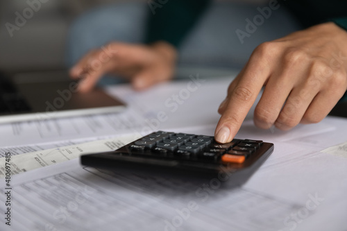 Crop close up young woman using calculator  reviewing utility bills or taxes  managing household monthly budget  accounting or making financial audit in computer application  savings concept.