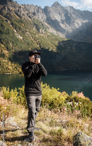 Young man photographer taking photographs with digital camera in a mountains.