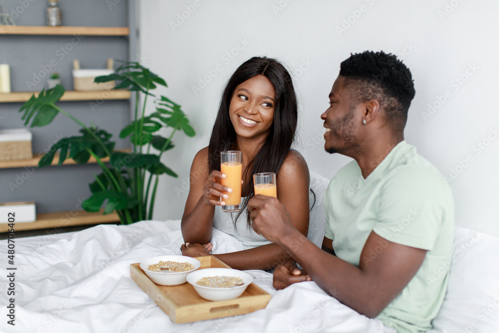 Happy pretty young african american woman and man woke up after night sleep on bed in bedroom have healthy breakfast Happy pretty young african american woman and man woke up after night sleep on bed in bedroom have healthy breakfast