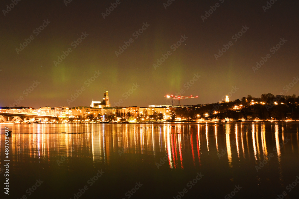 Fototapeta premium Beautiful night view of Stockholm City when the phenomena northern lights is displayed. Northern lights, or polar lights, over Stockholm skyline on a winter night. Photo taken January 15, 2022.