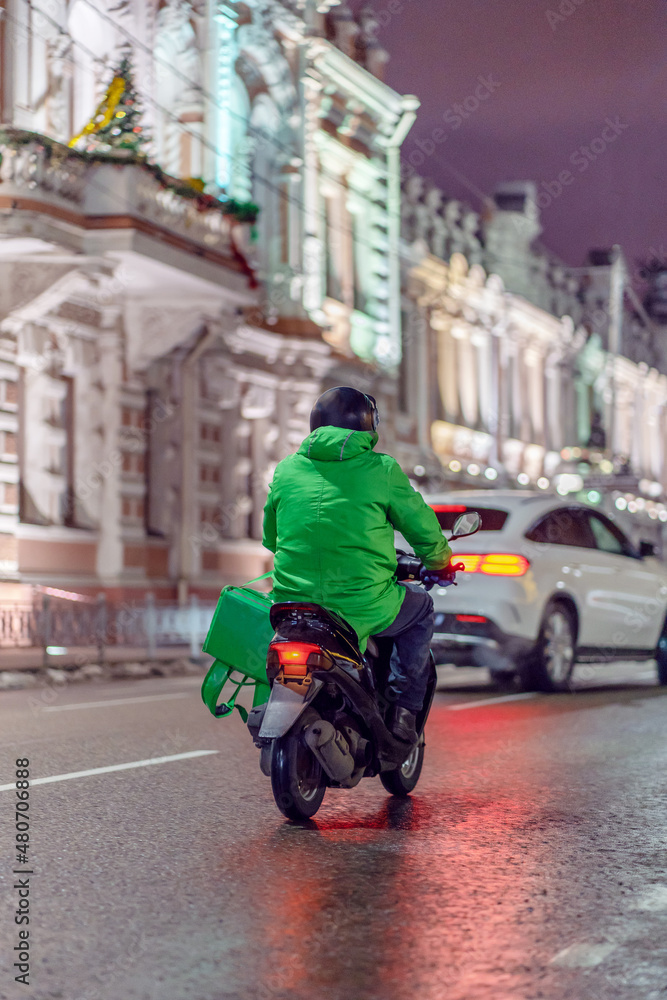 Food delivery boy on scooter at night with isothermal food case.