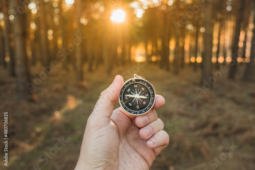 a hand holding a compass seeking orientation in the forest at sunset. Concept of orientation and leadership
