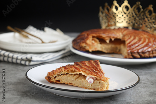 A cut piece of traditional French galette des rois or King cake, with fève inside. Cake made with puff pastry and creamy almond filling roll in circles shape. It's associated with Epiphany 