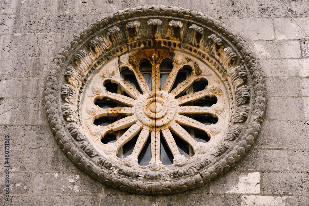 Rose window with ornaments and patterns on the dark stone wall of the church