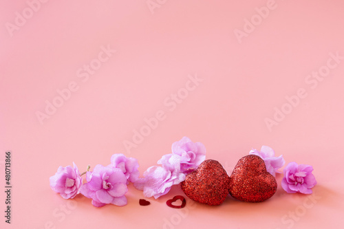 Valentines, love and wedding concept. Lilac violet flowers and red hearts on pink background. Copy space.