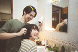Young adult asian couple man and woman dressing hair with hairdryer blowing. Together care at home in bathroom.