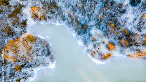 Drone view of a river with an icy lake on a snowy forest plain during a clear winter morning and bright sunrise