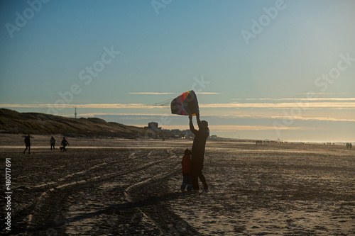Father and son flying kite together on the beach in winter sunshine