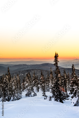 Sheregesh. Russia. Bright orange sunset among the mountains and snow-covered trees. Winter