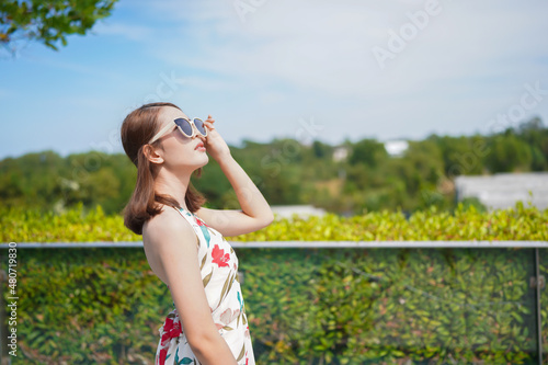asian woman wearing a floral dress wear sunglasses standing outdoors Holiday fun, holiday fashion concept © SKW