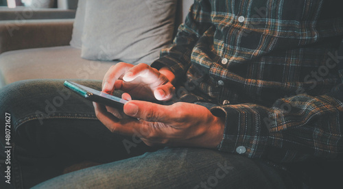 Принти на полотні young man in smart casual wear holding smart phone and looking at it while sitting at his working place in coffee shop