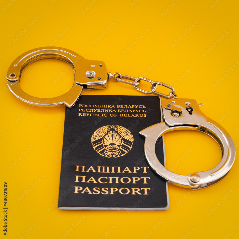 Passport of a citizen of the Republic of Belarus and handcuffs on an orange background. Close-up. Passport of a citizen of the Republic of Belarus and handcuffs on an orange background. Close-up.