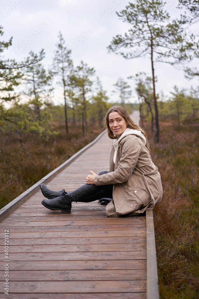 Fototapeta premium Lifestyle photo A girl trench coat in nature. viru bog trail in Estonia. Travel, exploration, healthy lifestyle, active rest