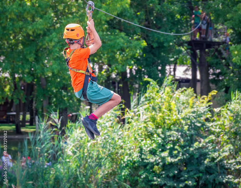 Back view with a teen young adult riding a zip line in Comana Adventure Park, Romania.